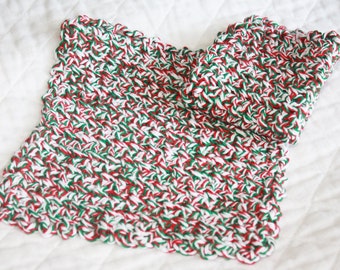May include: A hand-crocheted scarf in red, green, and white. The scarf has a rectangular shape with a scalloped edge. The yarn is tightly woven, giving a textured look. The colour scheme suggests a festive or winter theme, suitable for the colder months.
