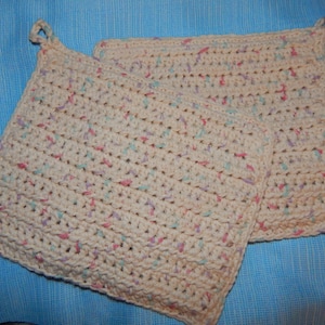 May include: Two crocheted pot holders in a cream color with pink, blue, and green accents. The pot holders are made with a simple stitch pattern and have a loop for hanging.