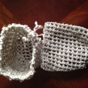 May include: Two crocheted beige scrubbies, one is a round shape and the other is a flat oval shape.