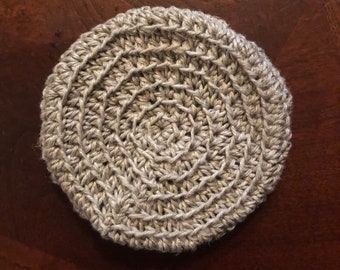 May include: A round, crocheted coaster in a light beige color. The coaster has a circular pattern with a raised center.