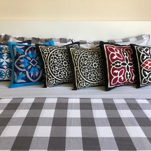 May include: Five decorative throw pillows with geometric patterns. The pillows are arranged on a gray and white checkered bedspread. The pillows are black, blue, and red with white accents.