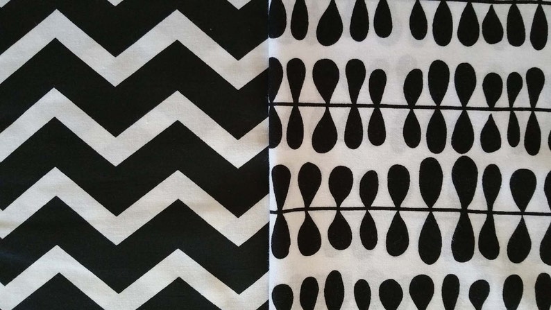 May include: Black and white fabric with two different patterns. One side has a chevron pattern and the other side has a repeating teardrop pattern.