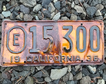 May include: A vintage California license plate from 1936. The plate is rusty and faded, with the number "E 15 300" printed in black on a yellow background.