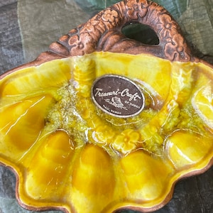 May include: A yellow ceramic dish with a brown handle and a flower design. The dish has six sections and is labeled "Treasure-Craft of Hawaii, Maui, Hawaii".