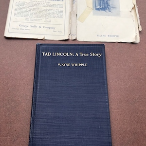 May include: A navy blue hardcover book with the title "TAD LINCOLN: A True Story" and the author's name "WAYNE WHIPPLE" printed in gold lettering.
