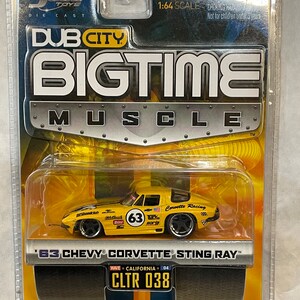 May include: A yellow 1963 Chevrolet Corvette Sting Ray die-cast model car with black wheels and racing decals. The car is in a clear plastic display case with a black and yellow background. The packaging includes the text "Dub City Bigtime Muscle" and "Wave California 04 CLTR 038".