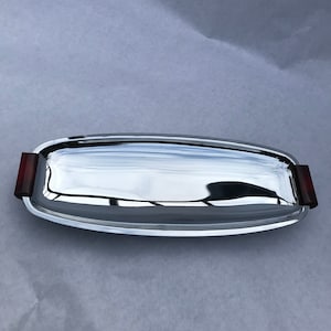 May include: A silver serving tray with a rectangular shape and rounded edges. The tray has two dark red plastic handles on either side.