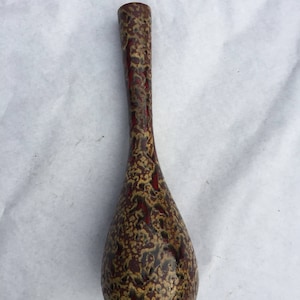 May include: A tall, slender vase with a bulbous base and a narrow neck. The vase features a speckled pattern in shades of brown, red, and gold. The vase is likely made of ceramic or pottery and is suitable for displaying flowers or as a decorative item.