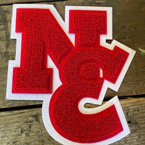 May include: Red felt letter patch with white outline, spelling out the letters "NC".