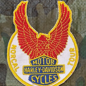May include: Embroidered patch featuring a red eagle with yellow detailing, the words "NORCAL TOUR" and "MOTOR HARLEY-DAVIDSON CYCLES" in blue and yellow. The patch is circular with a yellow border.