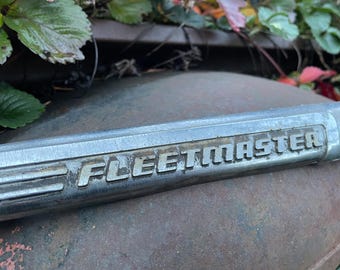 May include: Close-up of a silver metal trim piece with the word "FLEETMASTER" embossed on it.