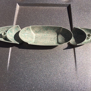 May include: Set of four white ceramic candle holders with a speckled green and white glaze. The holders are shaped like boats and have a hole in the center for a candle.