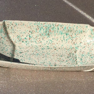 May include: A vintage serving dish set with a speckled pattern in white, teal, and red. The set includes a large oval tray and two smaller, nested dishes. The dishes have a mid-century modern design.