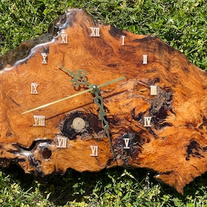 May include: A wooden clock with Roman numeral markings on a natural wood slice. The clock face is brown with dark brown streaks and the hands are gold.