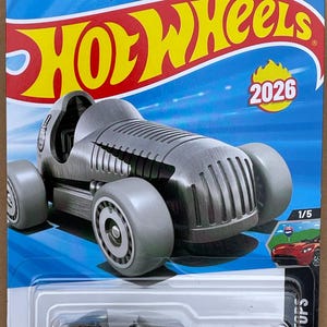 May include: A gray Hot Wheels die-cast toy car. The car is a vintage-style racer with large wheels and a streamlined body. The packaging includes the Hot Wheels logo, the number 2026, and the text "90 YEARS".