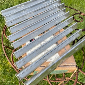 May include: A collection of silver-colored, rectangular metal bars, labeled "LEAD FREE J-STD", are stacked on top of a cardboard box. The bars are arranged in parallel, with the text visible on each. The background is a rusty metal table.