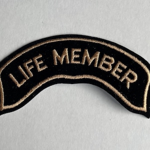 May include: Black and gold embroidered patch with the text "LIFE MEMBER" in a curved shape.