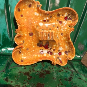 May include: A vintage ceramic ashtray with a brown and white speckled glaze and red accents. The ashtray has a unique, asymmetrical shape with a scalloped edge.