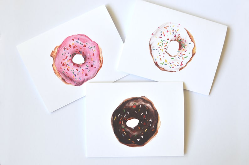 May include: Three blank greeting cards with illustrated donuts. The donuts are pink with sprinkles, white with sprinkles, and chocolate with sprinkles.