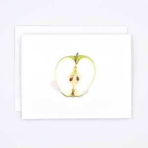 May include: A watercolour painting of a green apple cut in half, showing the white flesh and brown seeds.