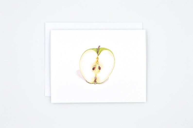 May include: A watercolour painting of a green apple cut in half, showing the white flesh and brown seeds.