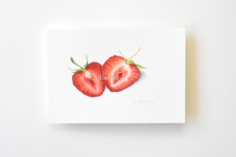 Op de afbeelding: Waterverf schilderij van twee gehalveerde aardbeien, geschilderd in tinten rood en groen. De aardbeien zijn op een witte achtergrond met de handtekening van de kunstenaar rechtsonder.