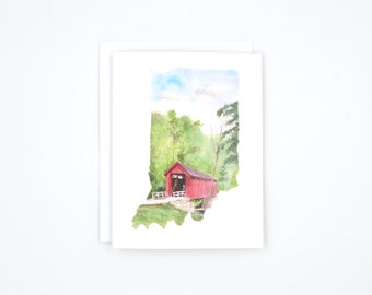 May include: A watercolor painting of a red covered bridge in the shape of the state of Indiana. The bridge is surrounded by green trees and a blue sky.