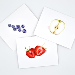 May include: Three cards with watercolour illustrations of fruit. The first card shows a cluster of blueberries. The second card shows a green apple cut in half. The third card shows two halves of a strawberry.