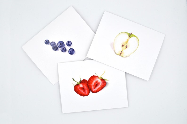 May include: Three cards with watercolour illustrations of fruit. The first card shows a cluster of blueberries. The second card shows a green apple cut in half. The third card shows two halves of a strawberry.
