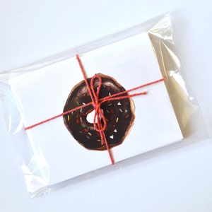 May include: A white card with a red and pink string tied around it. The card has a drawing of a chocolate donut with colorful sprinkles on top.