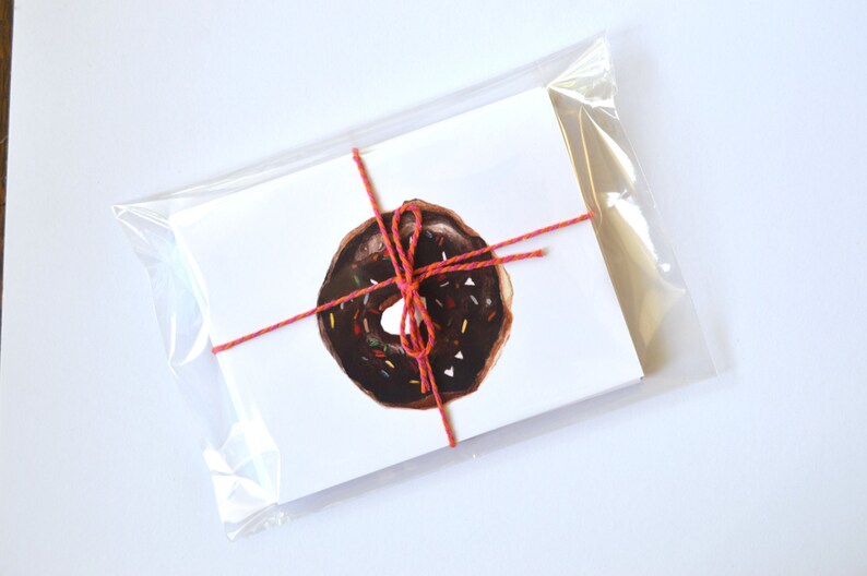 May include: A white card with a red and pink string tied around it. The card has a drawing of a chocolate donut with colorful sprinkles on top.
