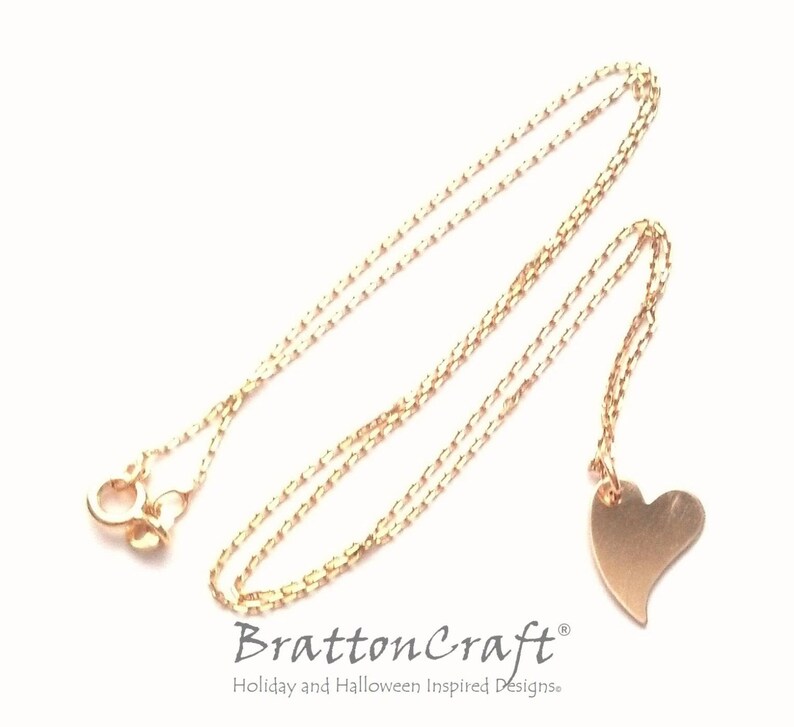May include: A gold chain necklace with a small, brushed gold heart pendant. The chain is a delicate, box style chain.