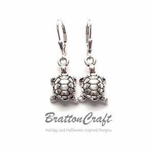 May include: Silver turtle dangle earrings with a textured shell design. The earrings have a leverback closure.