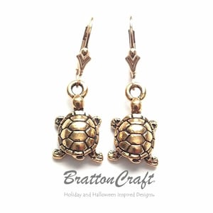 May include: Gold tone turtle dangle earrings with a hook closure. The turtles have a detailed shell design.