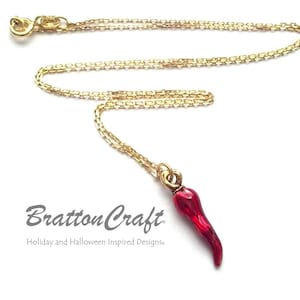 May include: A gold chain necklace with a red chili pepper charm. The charm is made of glass and has a shiny finish. The necklace is 18 inches long and is perfect for adding a touch of spice to any outfit.