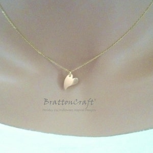 May include: A gold chain necklace with a small, flat, gold heart pendant. The necklace is on a model's neck.