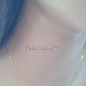 May include: A gold chain necklace with a heart pendant. The necklace is worn by a person with dark hair. The text "BrattonCraft" and "Holiday and Halloween Inspired Designs" is visible on the image.