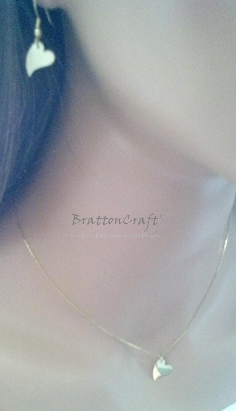 May include: A gold chain necklace with a heart pendant. The necklace is worn by a person with dark hair. The text "BrattonCraft" and "Holiday and Halloween Inspired Designs" is visible on the image.