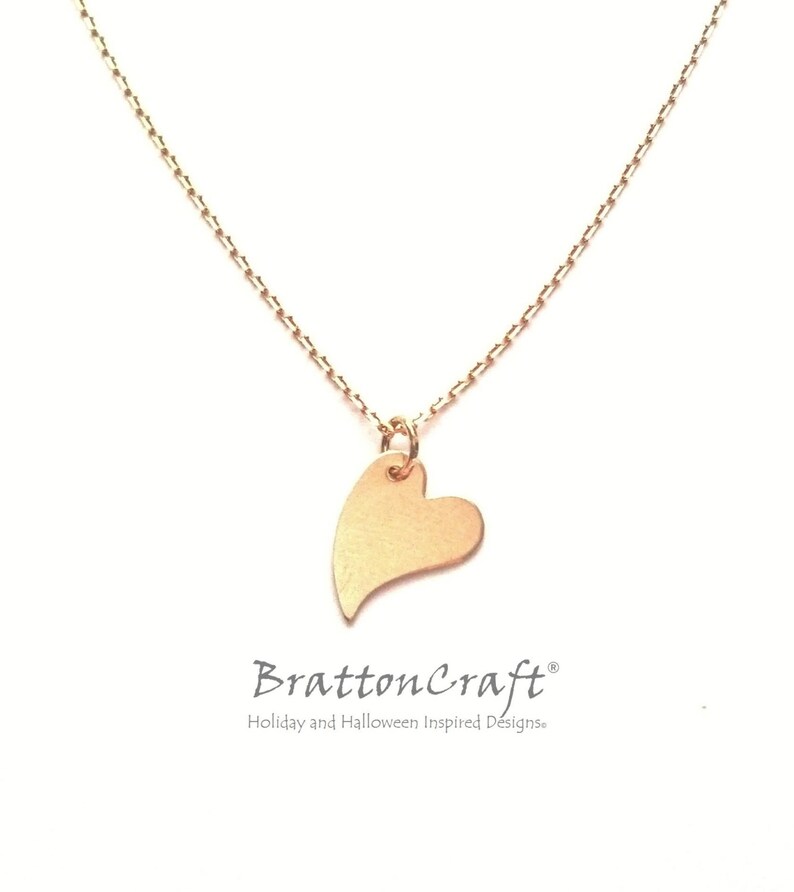 May include: A delicate gold chain necklace with a small, heart-shaped pendant. The pendant is a simple, smooth design with a slightly pointed tip.