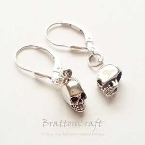 May include: A pair of silver skull dangle earrings with leverback closures. The skulls are detailed and have a slightly textured finish.