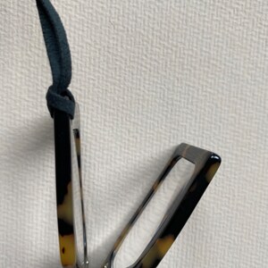 May include: A tortoiseshell folding reading glasses with a black leather cord.