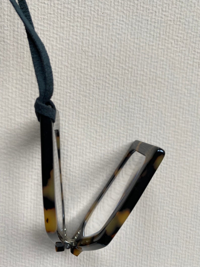 May include: A tortoiseshell folding reading glasses with a black leather cord.