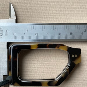 May include: A close-up of a tortoiseshell eyeglasses frame being measured with a ruler. The ruler shows the frame is approximately 5.5 cm wide.