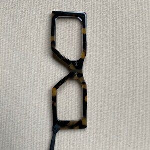 May include: Tortoise shell reading glasses with a black cord. The glasses have a unique geometric shape.