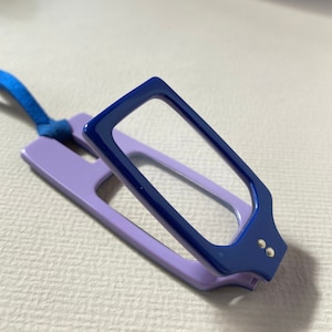May include: A blue and purple magnifying glass with a handle and a blue ribbon attached. The magnifying glass is folded closed.