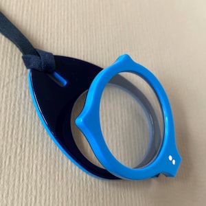May include: A pair of blue and navy blue eyeglasses with a matching strap. The glasses have a unique, rounded shape with a light blue frame and clear lenses. The navy blue portion has a hole for the strap.