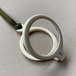 May include: White plastic reading glasses with a green cord. The glasses have a round frame and a small, round lens.