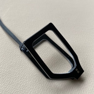 May include: Black magnifying glass with a black cord and two small black dots on the side.