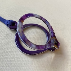 May include: A purple and white patterned magnifying glass with a blue cord.