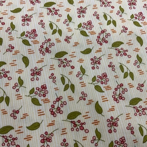 Puede incluir: Una tela blanca con un patrón repetido de pequeñas bayas rojas y hojas verdes sobre un fondo blanco. La tela tiene un sutil patrón a rayas de color marrón claro.